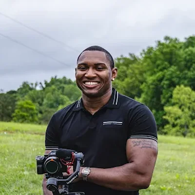 Mark Camp, smiling, holding a camera outdoors